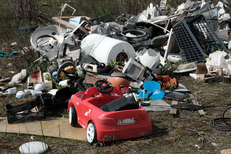 A large quantity of mixed household and retail waste spread across a floor surface, including crumpled paper, plastic bottles with labels, cardboard packaging, and various discarded containers. The pl